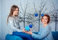 Happy smiling mother and daughter, holding gift box, sitting on the sofa with Christmas decorations Royalty Free Stock Photo